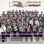 Full corps photo - in a stadium with flags behind the members.