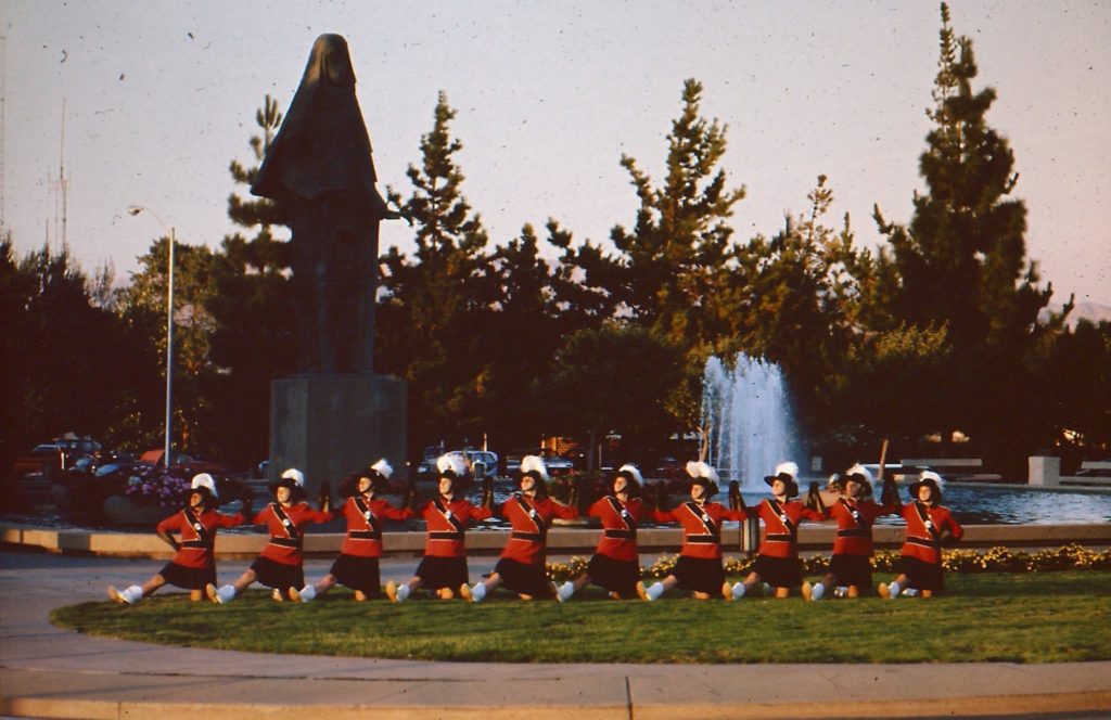 Color guard doing a step of the bottle dance in front of a fountain